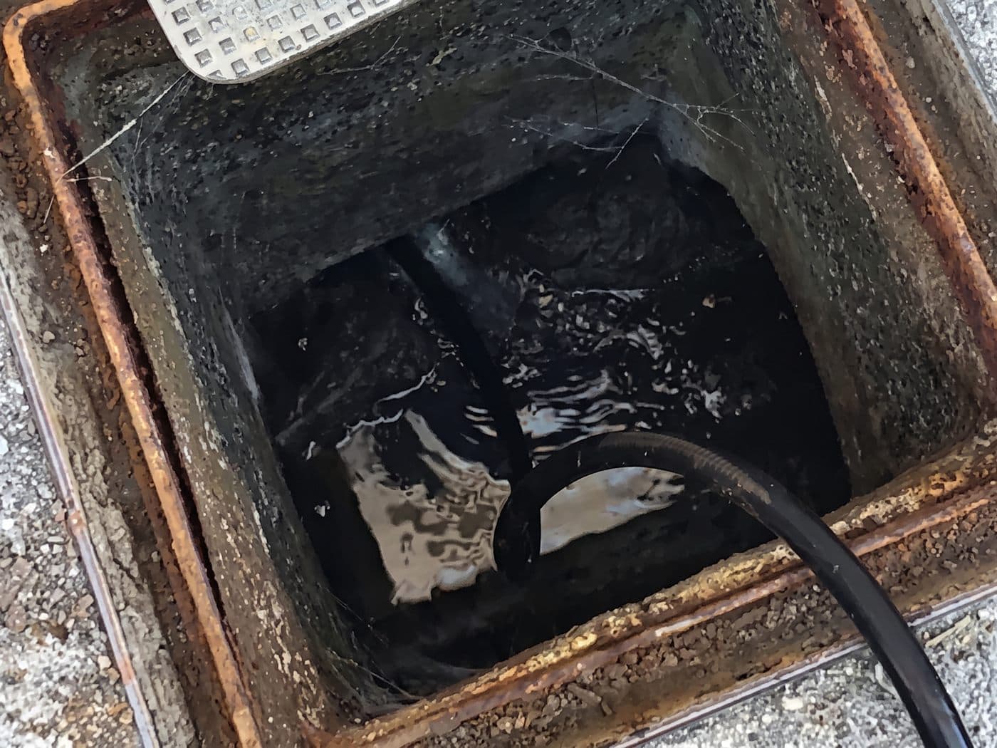 Cámara de alcantarillado abierta con el agua detenida y una manguera negra entrando