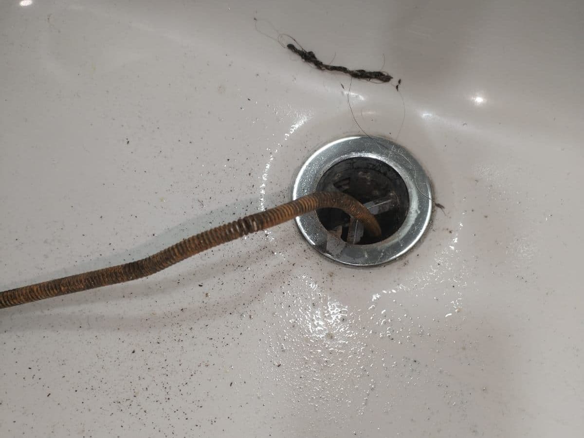 Sonda entrando por el desagüe de un lavamanos, con el pelo que salió del destape sobre la loza
