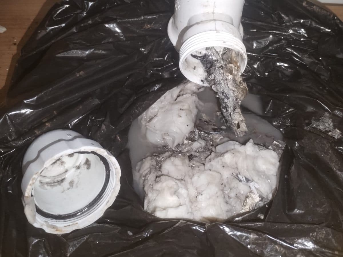 Sifón de un lavaplatos desarmado sobre una bolsa, con la grasa endurecida que tapaba el desagüe