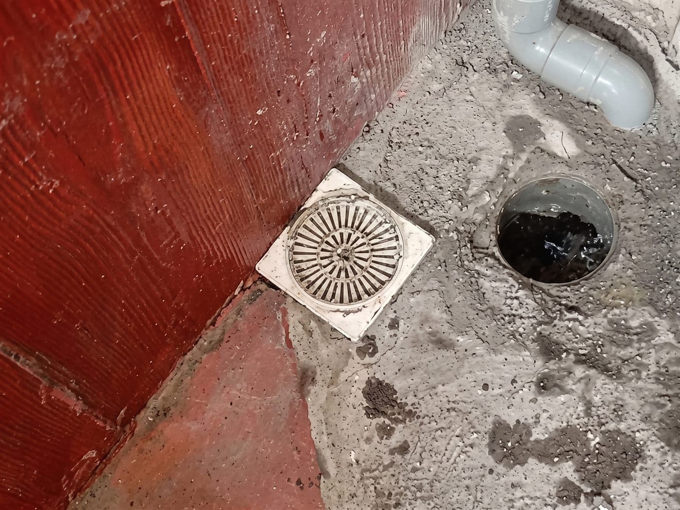 Rejilla de la pileta de un patio y, al lado, una boca de desagüe abierta