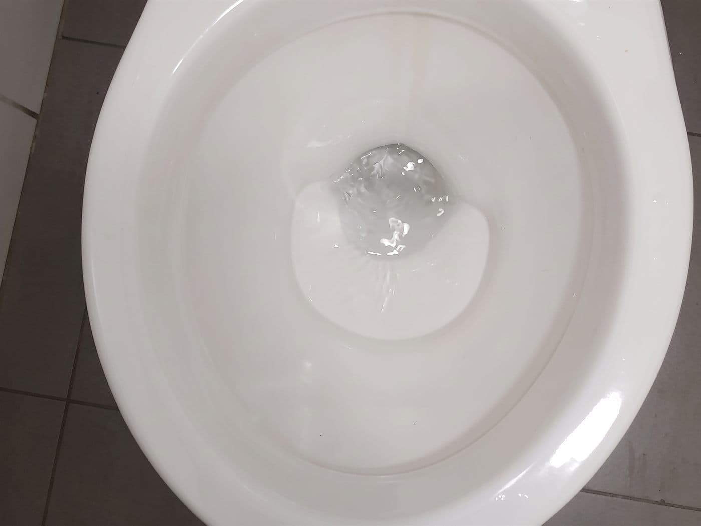 Taza de un WC vista desde arriba, con el agua bajando limpia por el desagüe después del destape