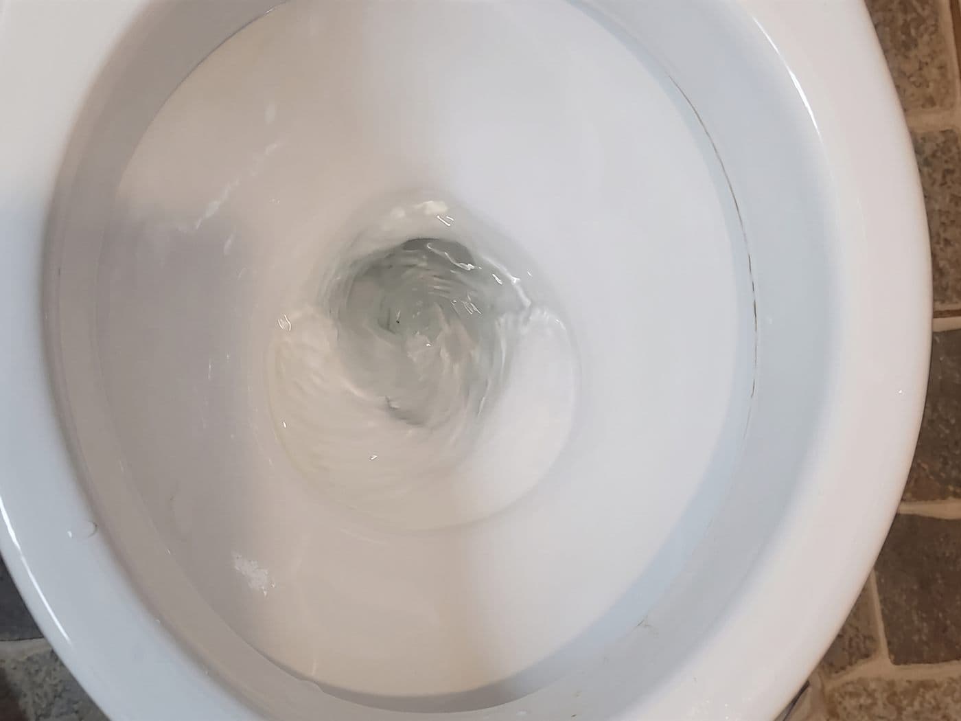 Agua girando hacia el desagüe de la taza de un WC al descargar, después del destape