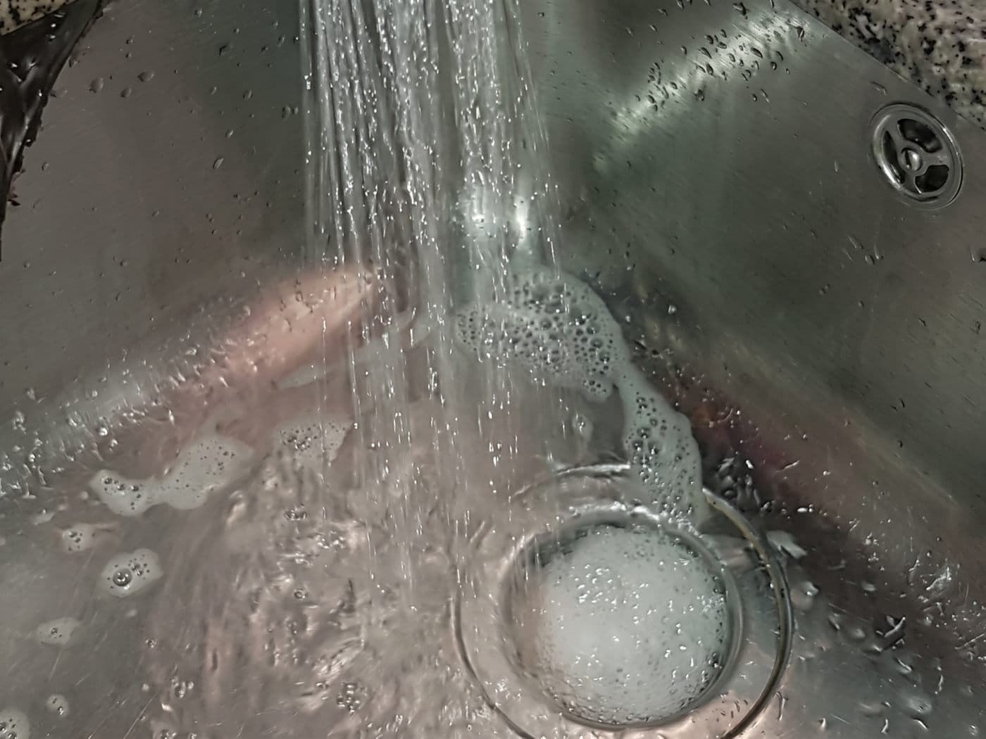 Agua de la llave bajando por el desagüe de un lavaplatos de acero, después del destape